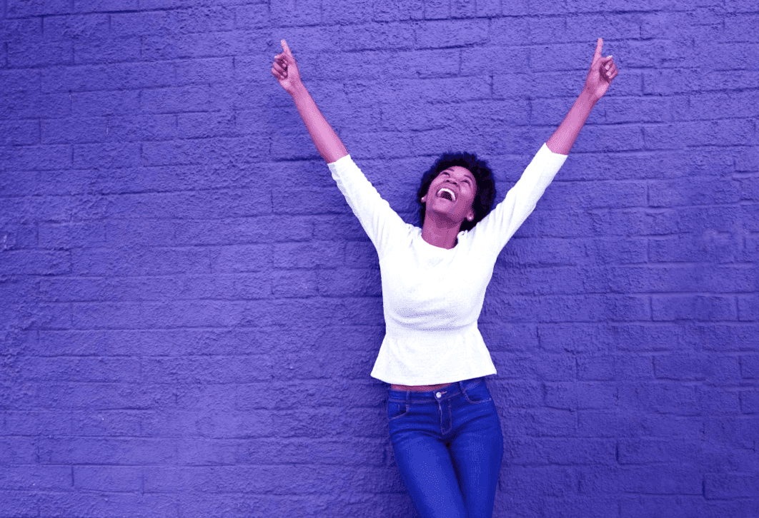 Person celebrating with raised arms against a purple brick wall